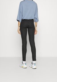 Svarta leggings med ett upprepande mönster, kombinerat med en lös blå topp och vita sneakers med inslag av grönt och gult.