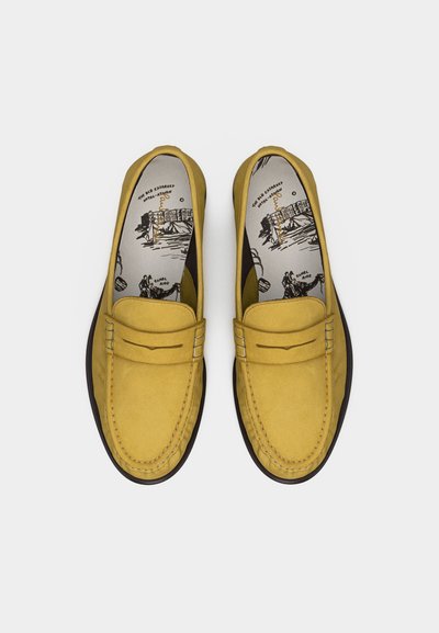 Mocassins en daim jaune avec des détails cousus et des semelles intérieures ornées d'illustrations en noir et blanc de désert et de promenade à dos de chameau.