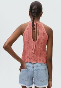 Virkat halter-top i dammig ros, med öppen rygg och satinband, samt texturerat stickat mönster. Bärs med ljusa denimshorts.