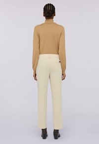 Maglione beige con collare alto, abbinato a pantaloni dritti color crema e stivali neri con tacco alla caviglia. Senza motivi o accenti visibili.