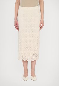 Jupe crayon en dentelle crème avec motif en crochets circulaires, ourlet festonné et design ajusté. Associée à des chaussures crème à bout pointu.