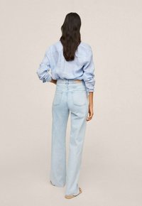 Jeans de tiro alto en azul claro con un diseño de pierna recta y bolsillos con solapa, combinados con una camisa azul a rayas semiestructurada.