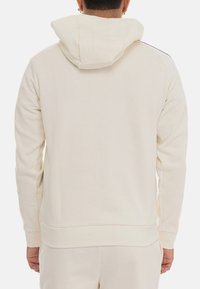 Felpa con cappuccio di colore crema chiaro, con una texture liscia, maniche lunghe e polsini a costine. Presenta una tasca a marsupio e cuciture laterali sottili.