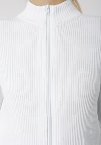 Top branco canelado com fecho de correr, apresentando uma gola alta e um fecho de correr frontal. O tecido tem uma superfície texturada com linhas horizontais subtis.