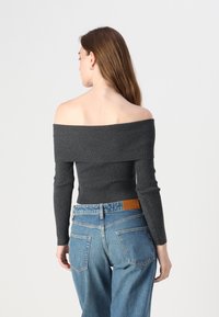 Top cinza de malha off-the-shoulder com mangas longas, combinado com jeans de ganga azul claro de cintura alta, com um patch de pele bege na cinta.