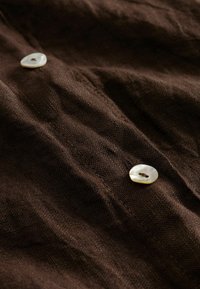 Gros plan sur un tissu texturé marron foncé avec deux petits boutons beiges cousus dessus.