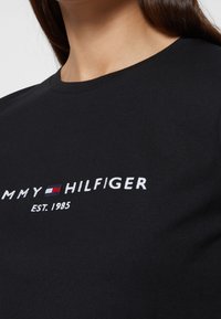 Černé bavlněné tričko s kulatým výstřihem, se všitým vyšitým textem a logem "TOMMY HILFIGER" v červené, bílé a modré.
