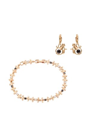 Złota bransoletka i kolczyki w kształcie kota z czarnymi i białymi kamieniami szlachetnymi na białym tle, podkreślające misterną pracę metalową i kamienie.