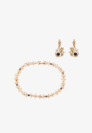 Złota bransoletka i kolczyki w kształcie kota z czarnymi i białymi kamieniami szlachetnymi na białym tle, podkreślające misterną pracę metalową i kamienie.