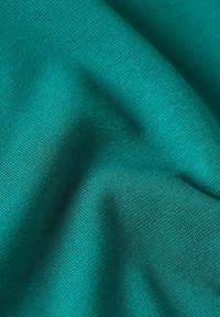 Teal stof med en struktureret vævning, der viser subtile variationer i lys og skygge. Blødt at røre ved med en glat, mat finish.