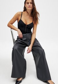 Bodice nero con spalline sottili e bottoni frontali, abbinato a pantaloni larghi in ecopelle nera. Tessuto liscio e vestibilità rilassata.