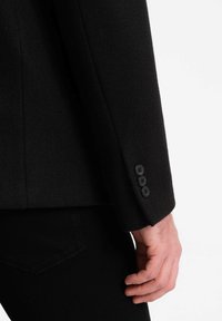 Zwarte wollen blazer in een mix met een soepele textuur, met een close-up van de mouw en drie knoopaccenten bij de manchetten.
