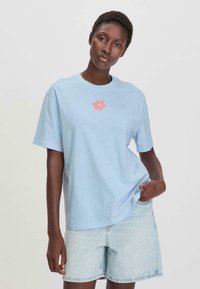 Lichtblauwe katoenen t-shirt met een ronde halslijn, korte mouwen en een roze bloemgraphic op de borst. Gecombineerd met lichtblauwe denim shorts.