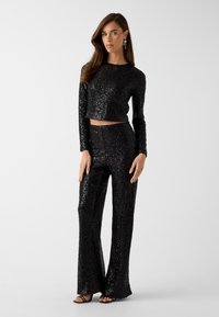 Ensemble noir en sequins composé d'un haut court à manches longues et d'un pantalon évasé, avec une texture brillante et une silhouette ajustée.
