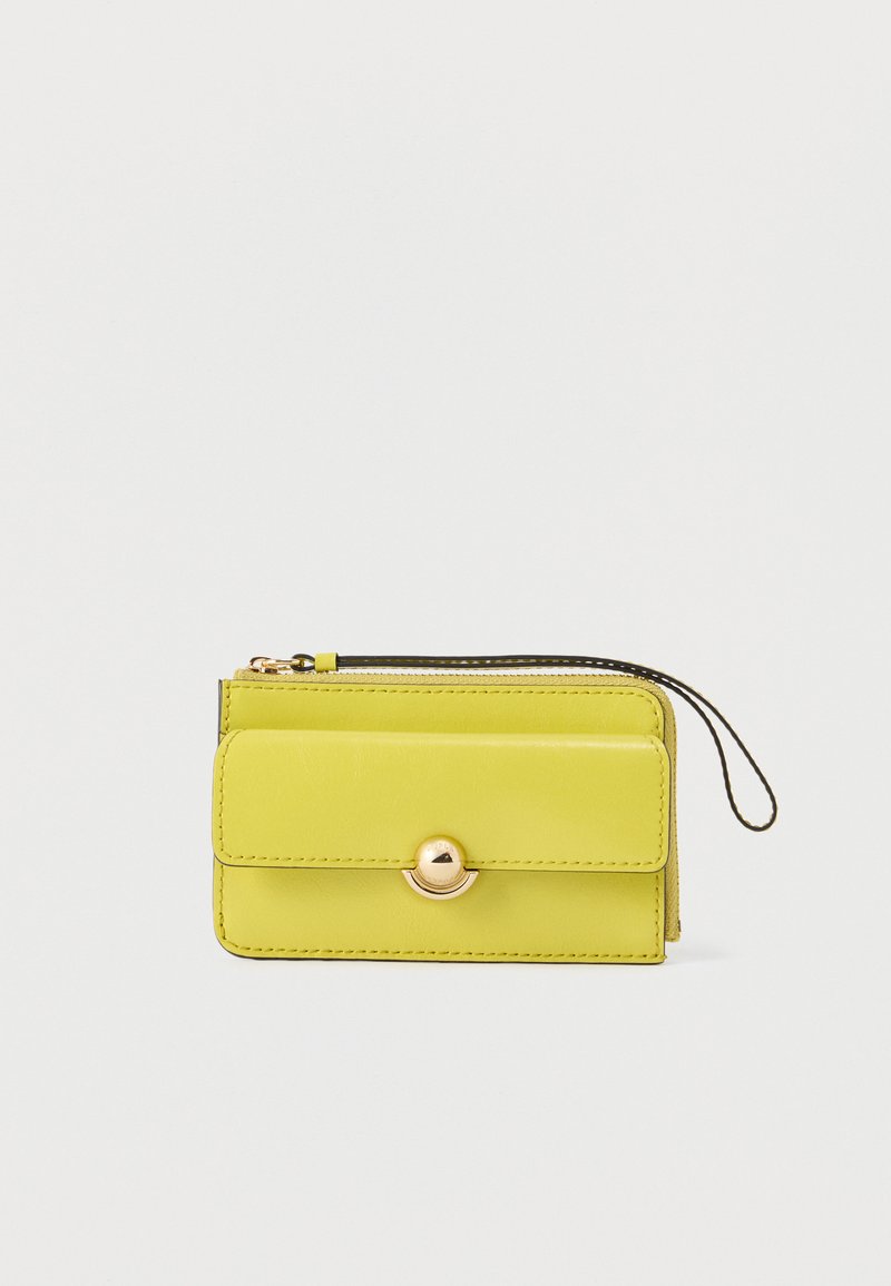 Petit portefeuille bracelet en cuir jaune avec rabat avant et bouton doré, fermeture éclair, et boucle de poignet noire sur fond blanc.