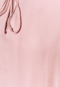 Tessuto rosa chiaro con una texture a righe diagonali, caratterizzato da un piccolo'apertura orizzontale e nastri al collo.