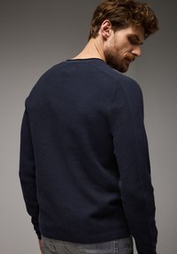 Tyrkysově modrý svetr s dlouhými rukávy, zdobený texturovaným ribbovaným vzorem. Kulatý výstřih a přiléhavé rukávy, stylizované zezadu.