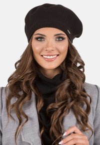 Beret negru tricotat, realizat dintr-un material moale, cu o formă rotundă. Modelul poartă o haină gri cu un pulover negru la gât.