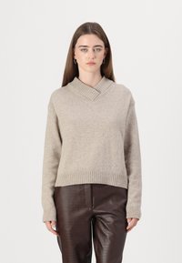 Pulover bej tricotat cu decolteu în V și tiv côtat, asociat cu pantaloni din piele maro cu textură de crocodil.