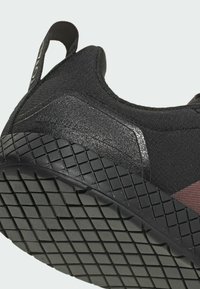 Zbliżenie na piętę czarnego buta sportowego z teksturowaną podeszwą i materiałową pętelką do przeciągania, z napisem "4.0 LIGHT DROP" na bocznej części.