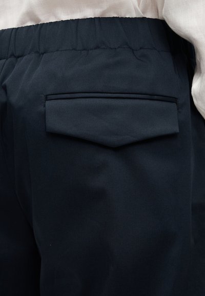 Παντελόνια σε ναυτικό μπλε χρώμα με πίσω τσέπη που έχει λεπτομέρεια με μυτερό καπάκι. Το υλικό είναι λείο με διακριτική λάμψη, με εμφανές ελαστικό ζωνάρι στη μέση.