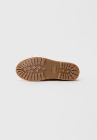 Semelle d'une chaussure en caoutchouc brun avec des rainures profondes et des grips en forme de croix, nom de la marque "FRIBOO" embossé près du talon.