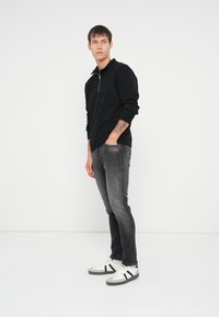 Sudadera negra con cremallera, jeans ajustados grises y zapatillas blancas con rayas negras. Textura suave, diseño casual y silueta ajustada.