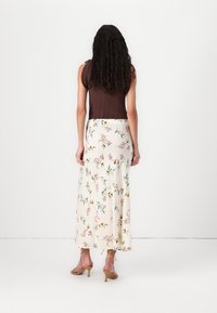 Brun, ermeli topp kombinert med en flytende, blomsterprydd kremfarget maxiskjørt. Det lyse blomsterdesignet har rosa og gule detaljer.