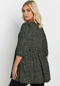 Blusa nera con pois bianchi, maniche a sbuffo e vita arricciata, caratterizzata da un design fluido e una vestibilità comoda.