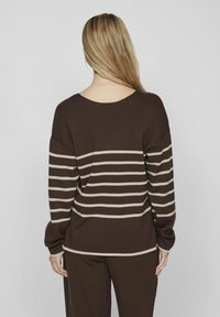 Pull en tricot marron avec de larges rayures horizontales beiges, doté d'un décolleté plongeant dans le dos et de manches amples. Texture accentuée.