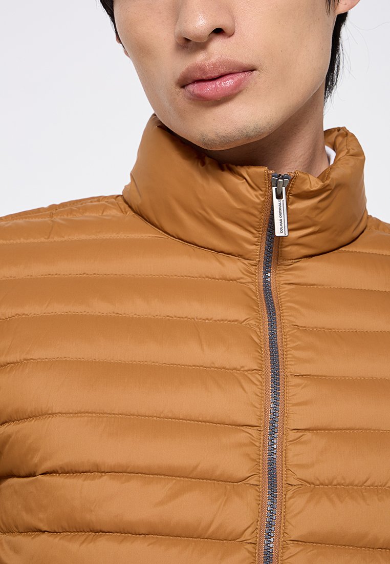 Giacca a vento color rame con texture trapuntata, colletto alto e zip frontale. Il materiale appare liscio e leggero.