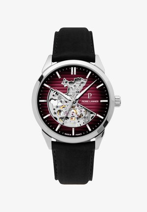 Strieborné a čierne hodinky s vínovo číslom na ciferníku, čiastočný skeletový dizajn ukazujúci ozubené kolieska, strieborné hodinové značky a čierny kožený remienok.