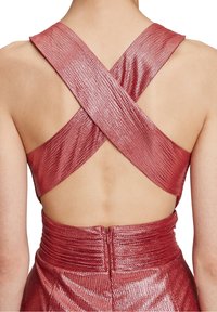 Röd metallisk klänning med en korsad ryggdesign, texturerad tyg med en glänsande yta och samlade detaljer vid midjan.