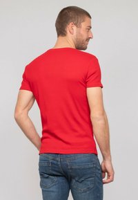 T-shirt rouge ajustée à manches courtes en tissu lisse, assortie à un jean en denim bleu avec poches arrière et une texture légèrement usée.