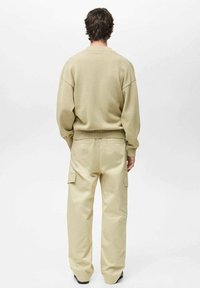 Beige stickad tröja med ribbade muddar och nederkant, kombinerad med ljusbeige cargobyxor med sidofickor och en avslappnad passform.