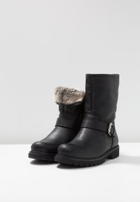 Black leather ankle boots with a textured exterior, faux fur cuff, strap accent, and rugged sole, designed for durability and comfort.