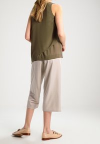 Olivgrön ärmlös topp, beige cropped byxor och ljusbruna loafers, med mjukt tyg och avslappnad passform med minimala designdetaljer.