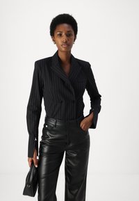 Blazer nero a righe sottili con design doppiopetto, abbinato a pantaloni in pelle nera a vita alta. Tessuto liscio e vestibilità su misura.