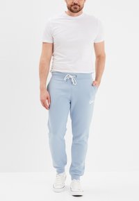 Lichtblauwe sweatpants met een witte trekkoord, nauwsluitende enkels en een klein wit logo op de linkerdij, gecombineerd met een eenvoudig wit t-shirt.