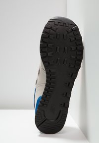 Sneaker grise avec une semelle extérieure en caoutchouc noir, des accents bleus et un motif de bande de roulement texturé. Doté d'un dessus en daim et d'un détail de marque contrastant.