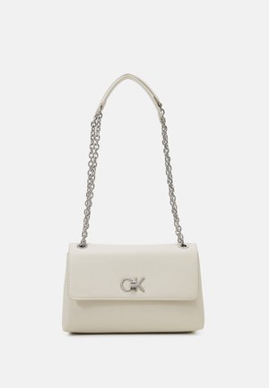 Sac à épaule couleur crème avec une bandoulière chaîne argentée et un logo CK argenté sur le rabat avant, sur un fond uni.