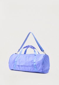 Κυλινδρική τσάντα τύπου duffel σε λιλά χρώμα, με διπλές λαβές χειρός και ρυθμιζόμενο ιμάντα ώμου, σε απλό φόντο.