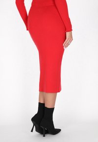 Rode geribbelde gebreide midirok, aansluitende silhouet, met een zoom net onder de knie, gecombineerd met zwarte stiletto enkelboots.