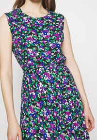 Kwiatowa sukienka na czarnym tle, z fioletowymi, białymi i zielonymi kwiatami. Posiada okrągły dekolt i pasek w talii.