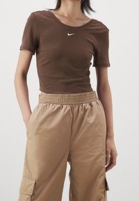 Braun gestreiftes, kurzes T-Shirt mit Rundhalsausschnitt und kurzen Ärmeln, mit einem weißen Nike-Logo. Getragen mit beigen Cargo-Hosen mit elastischem Bund.