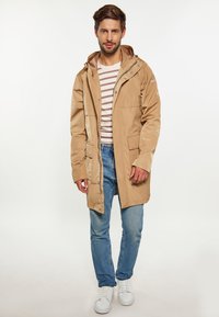 Bežinė vandeniui atspari striukė su kapišonu, spaudėmis ir dviem priekinių kišenių. Dėvima virš dryžuoto marškinėlio, derinama su mėlynomis džinsomis ir baltais sportbačiais.