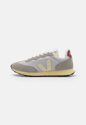Sneaker beige e grigio con tomaia in mesh, dettagli in suede, suola color crema e tab posteriore color bordeaux. Include un logo prominente sul lato.