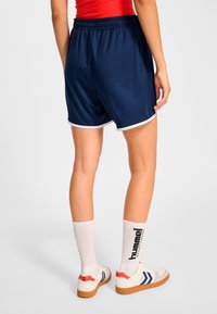 Marinblå sportshorts med vit kant, resårmidja och avslappnad passform, kombinerade med vita strumpor och sneakers i retrostil.