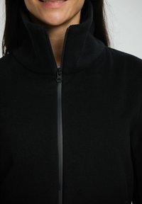 Sort fleecejakke med høj krave og fuld lynlås, der har en glat tekstur og et minimalistisk design.