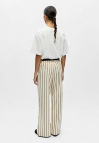 T-shirt en coton blanc à manches retroussées, associé à un pantalon large beige à rayures, doté d'une ceinture noire et de poches arrière.